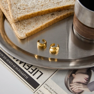 Golden stainless steel ear clips on a metal tray with a lifestyle aesthetic background