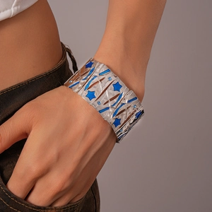 Detail of wide silver metal cuff bracelet featuring blue stars and enamel patterns