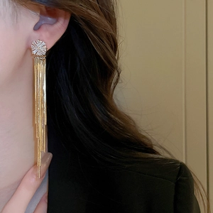 Close-up of elegant gold tassel earrings with zircon flower studs worn by a model