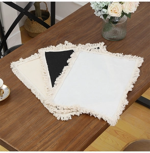 Close-up of beige, black and white linen placemats with soft fringe on a wooden table