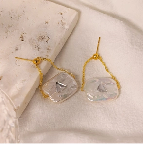Detailed close-up of Baroque pearl earrings with golden chain and triangular zircon stone