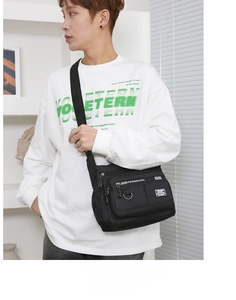 Detail of multi-pocket black nylon crossbody bag worn by model in a minimalist setting