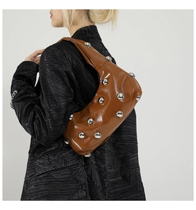 Detail view of brown glossy shoulder bag with large silver ball studs on model