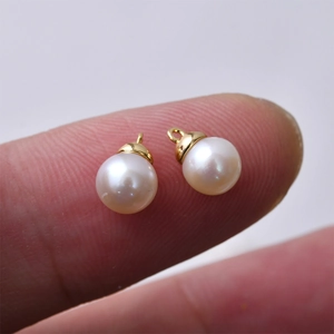 Detailed macro view of 6mm white freshwater pearl charms with gold loops on a fingertip