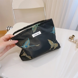 Detailed embroidery of blue and gold butterflies on a black jacquard makeup bag texture
