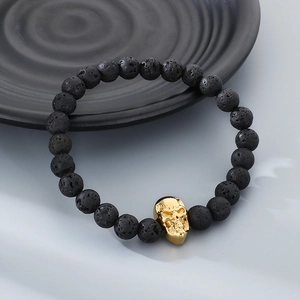 Macro shot of black lava rock beads and detailed gold skull charm on a dark beaded bracelet