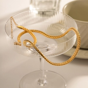 Golden woven stainless steel chain necklace with lobster clasp in a glass vase