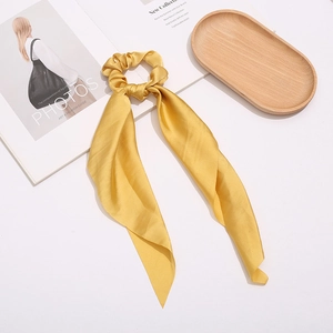 Detail of yellow satin hair scrunchie with long ribbon on a stylish magazine and tray