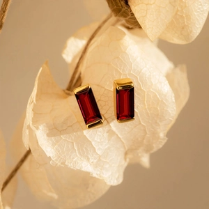Macro view of gold-plated square stud earrings featuring deep red rectangular zircon gems