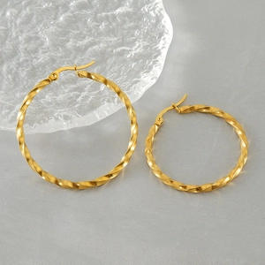 Golden French spiral twist hoop earrings in stainless steel on a soft textured background