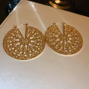 Detailed close-up of gold hollow disc earrings with intricate sunburst patterns