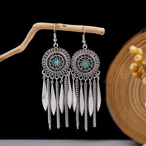 Detail of bohemian silver tassel earrings with turquoise bead on a rustic wooden stand