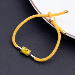 Close-up of yellow evil eye charm on adjustable woven rope bracelet with gold accents