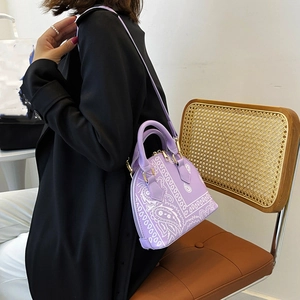 Close-up of a purple paisley shell handbag being worn with an adjustable crossbody strap