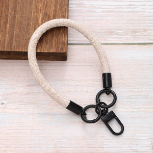 Beige woven wrist lanyard for phone with black metal lobster clasp on wood background