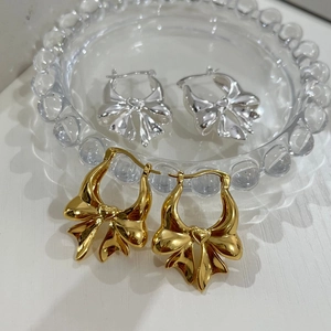 Detailed view of bow-shaped earrings in gold and silver finishes on a glass plate