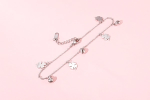 Detail of silver clover anklet with small bells and lobster clasp on pink background