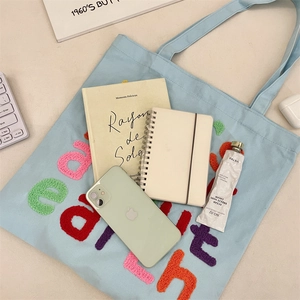 Detail of light blue canvas tote bag with colorful towel embroidered earth lettering