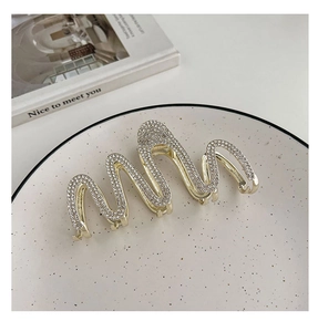 Detailed view of wave-shaped golden hair claw clip with sparkling rhinestones on a white plate