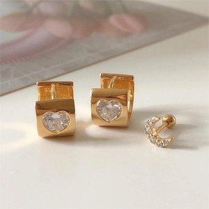 Detailed view of gold heart earrings and moon stud with white zirconia on white surface