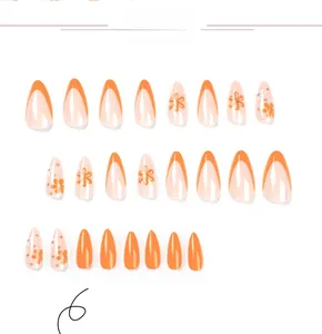 Detail view of long oval press-on nails featuring orange French tips and white flower designs