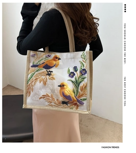 Detail of embroidered birds and flowers on a white linen tote bag worn by a model