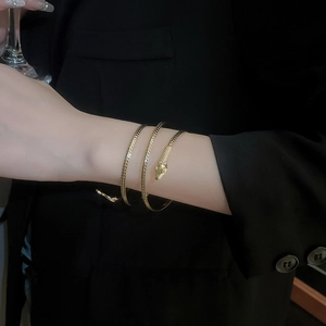 Detail of a gold snake wrap bracelet with scale texture worn by a model in black attire