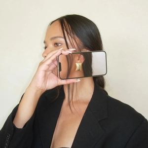 Macro detail of gold striped rectangular earrings worn with a chic black suit outfit