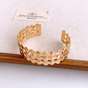 Macro shot of three-row gold oval beads hollowed out cuff bracelet on beige linen