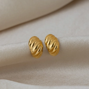 Close-up of gold-plated C-shape hoop earrings with ribbed texture on silk fabric