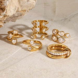 Set of five gold titanium steel geometric rings with zircons on marble stone background
