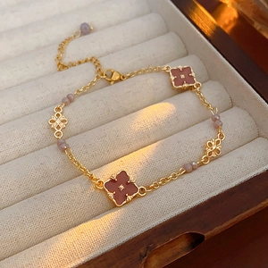 Detail of vintage gold bracelet with red clover and pink beads in a beige jewelry box