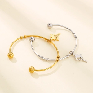 Detail of gold and silver open bangles with North Star charms on beige surface