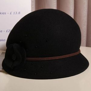 Dettaglio di cappello cloche in lana con cintura marrone, fiore 3D e perline nere decorative