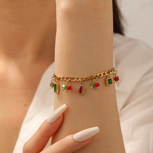 Detail of a gold-plated bracelet with red gemstone pendants and cherry beads on wrist