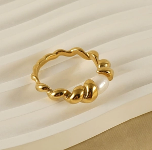 Detail of 18k gold wave band ring featuring a single white natural pearl on textured backdrop