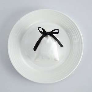 Detailed view of a white fabric drawstring pouch with a black ribbon bow on a ceramic plate