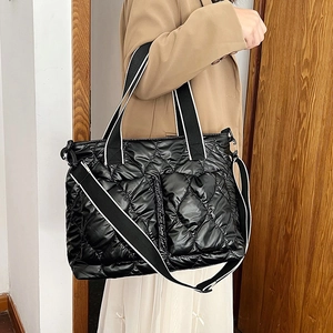 Detail of black quilted puffer tote bag with contrast woven straps and glossy fabric