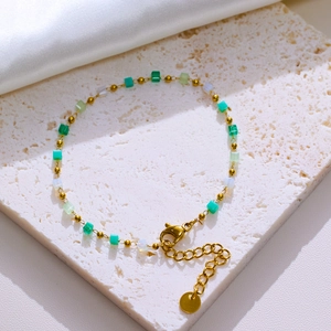 Golden chain bracelet with colorful cubic beads on a white textured stone pedestal