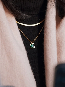 Detail of layered gold snake chain necklace with a rectangular emerald green zircon stone