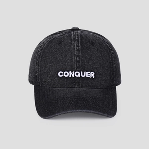 Detailed close-up of white 'CONQUER' embroidery on washed black cotton baseball cap