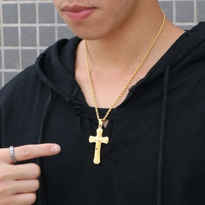 Close-up of a layered gold cross pendant with rope chain on a model wearing a ring