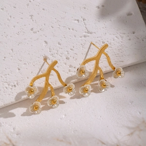Detail of 18K gold branch earrings with white flowers on a textured plaster background