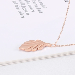 Détail d'un collier pendentif feuille en or rose sur une page de livre ouvert