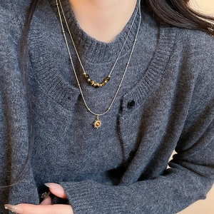 Detail of layered gold sun pendant necklace with tiger eye beads on model's neck