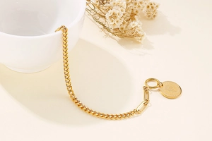 Detail of gold Cuban chain bracelet with Elizabeth II coin charm on white ceramic