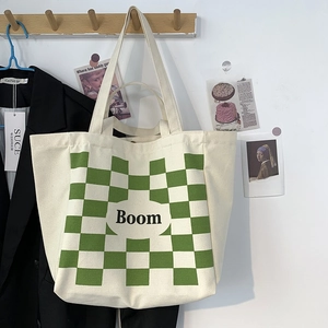 Close-up of cream canvas tote bag with green checkerboard pattern and Boom lettering