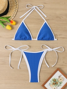 Flat lay of blue wavy textured bikini with white ties on wood with beach accessories