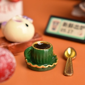 Close-up of miniature coffee cup set with golden spoon and green saucer for dollhouse