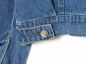 Close-up of metal buttons and contrast stitching on the blue denim jacket hemline